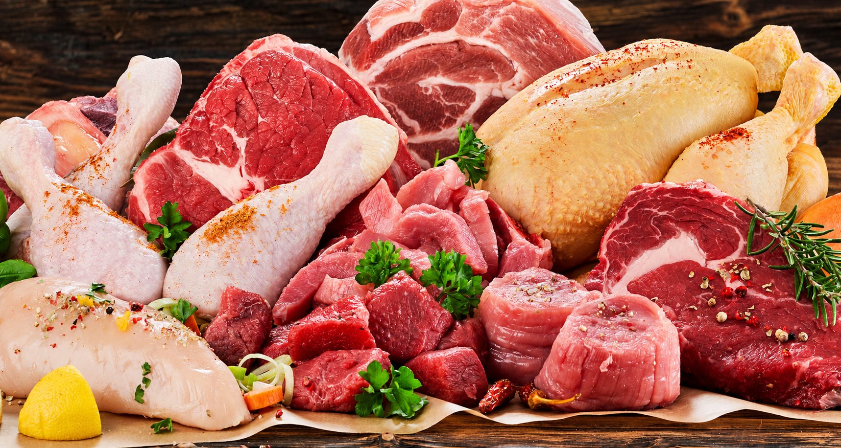 Assortiment de viandes crues comprenant des morceaux de bœuf, de porc, des cuisses de poulet et un poulet entier, garnis de persil, de romarin et d'épices sur du papier sulfurisé.