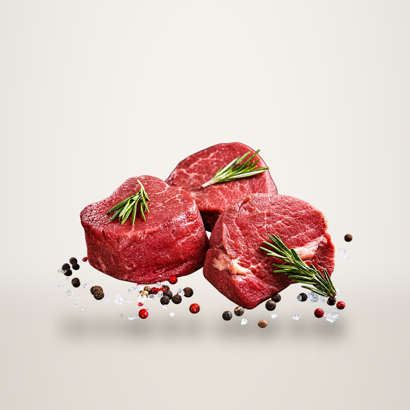 Trois médaillons de filet de bœuf cru garnis de brins de romarin, posés sur une ardoise noire parsemée de gros sel et de grains de poivre.